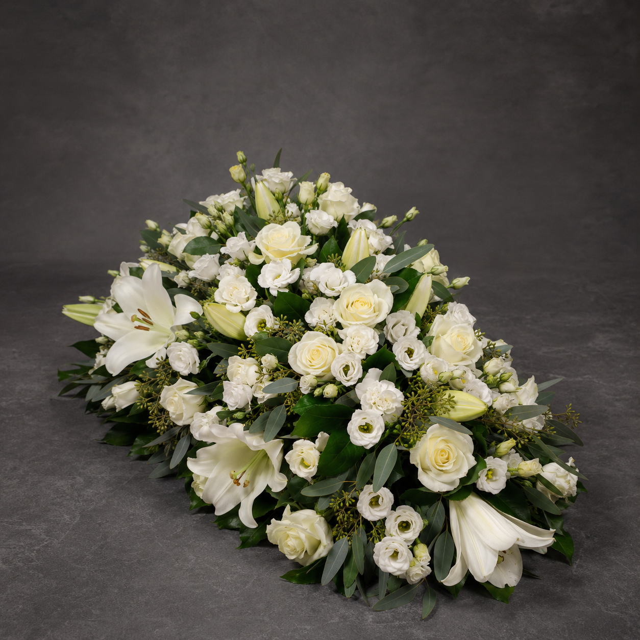 A large white floral arrangement featuring lilies, roses, and lisianthus with green foliage, photographed on a dark gray textured studio background.